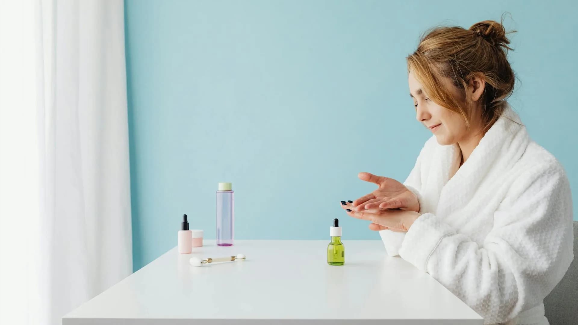 Pregnant woman in white bathrobe applying safe skincare products at table in bright studio